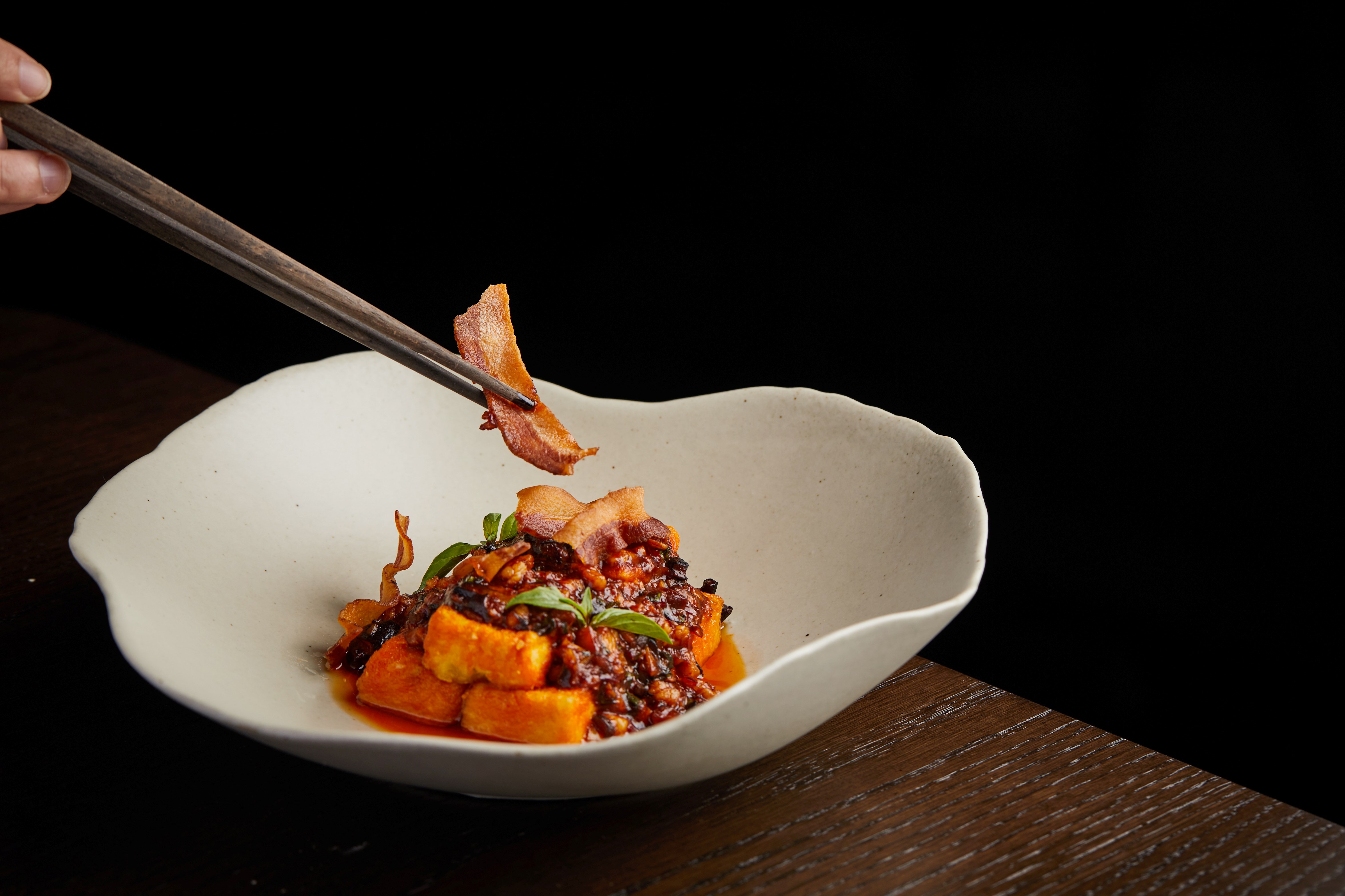 A person holding chopsticks over a bowl of food Description automatically generated